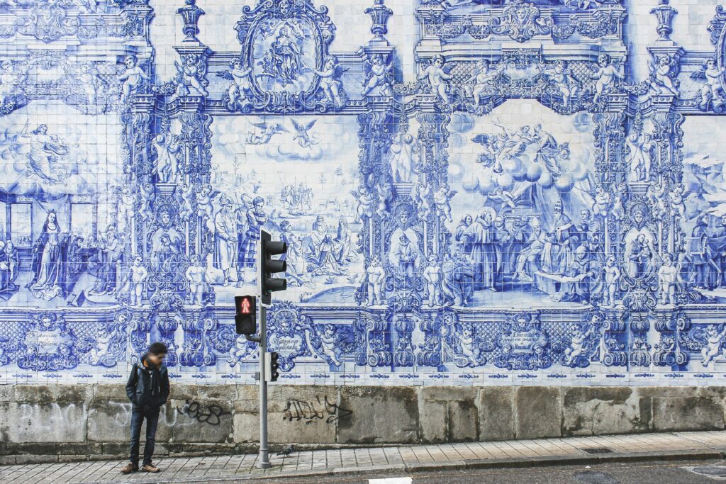 Man waiting for public transportation in Portugal with a blue and white mural behind him