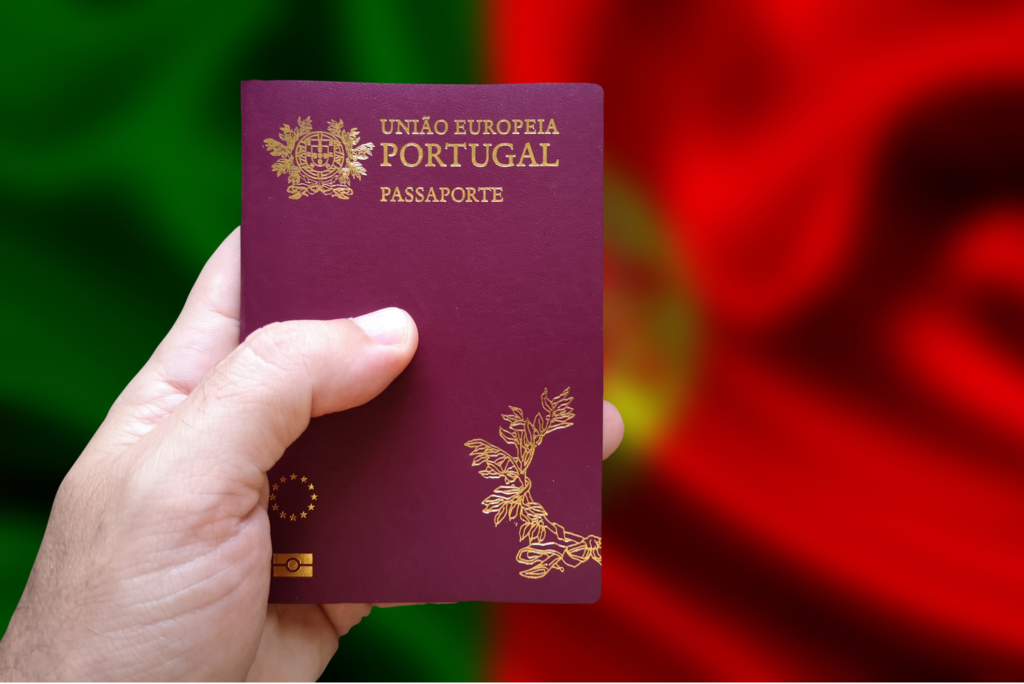 Hand holding a Portuguese passport with Portugal's flag in the background