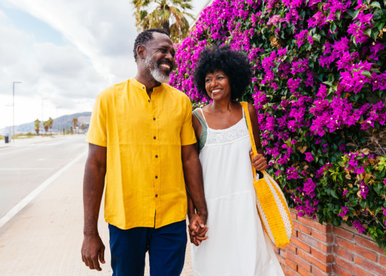 Retired couple smiling and holding hands on a bright street in Portugal