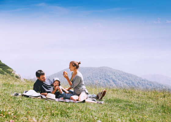 Young couple with small child eat a picnic lunch in Slovenian grassy hilly