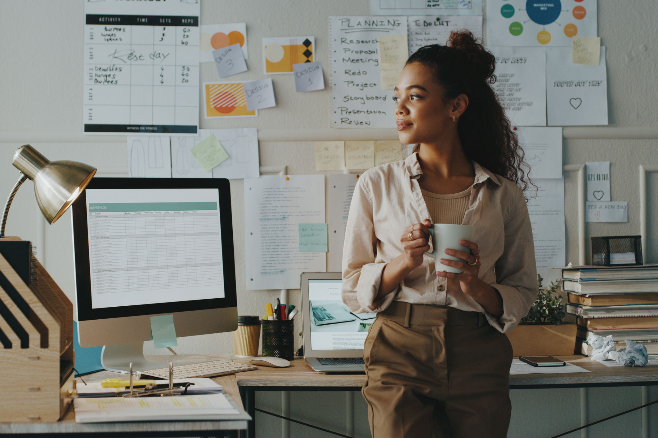 A professional woman looks confident standing by her computer with notes on the wall