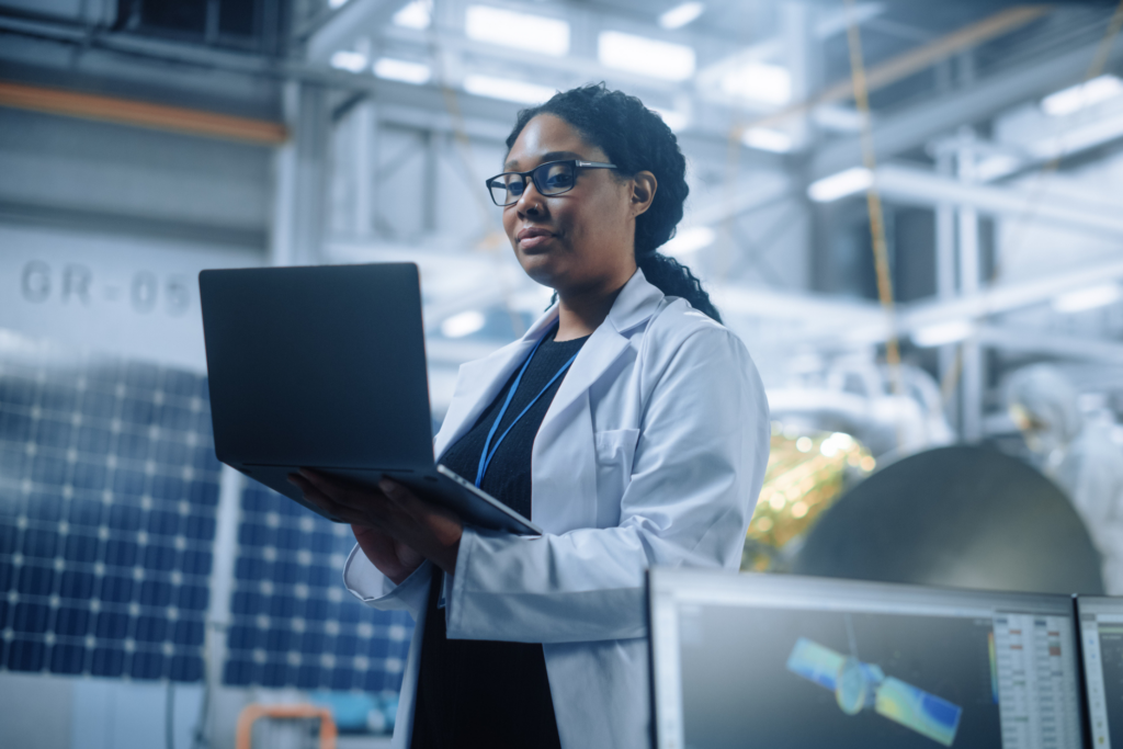 Woman wearing a white lab coat studies her work on a laptop in a science lab