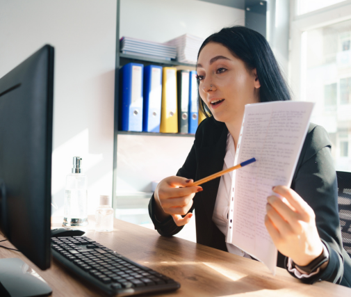 Woman pointing at a document looking at her computer screen