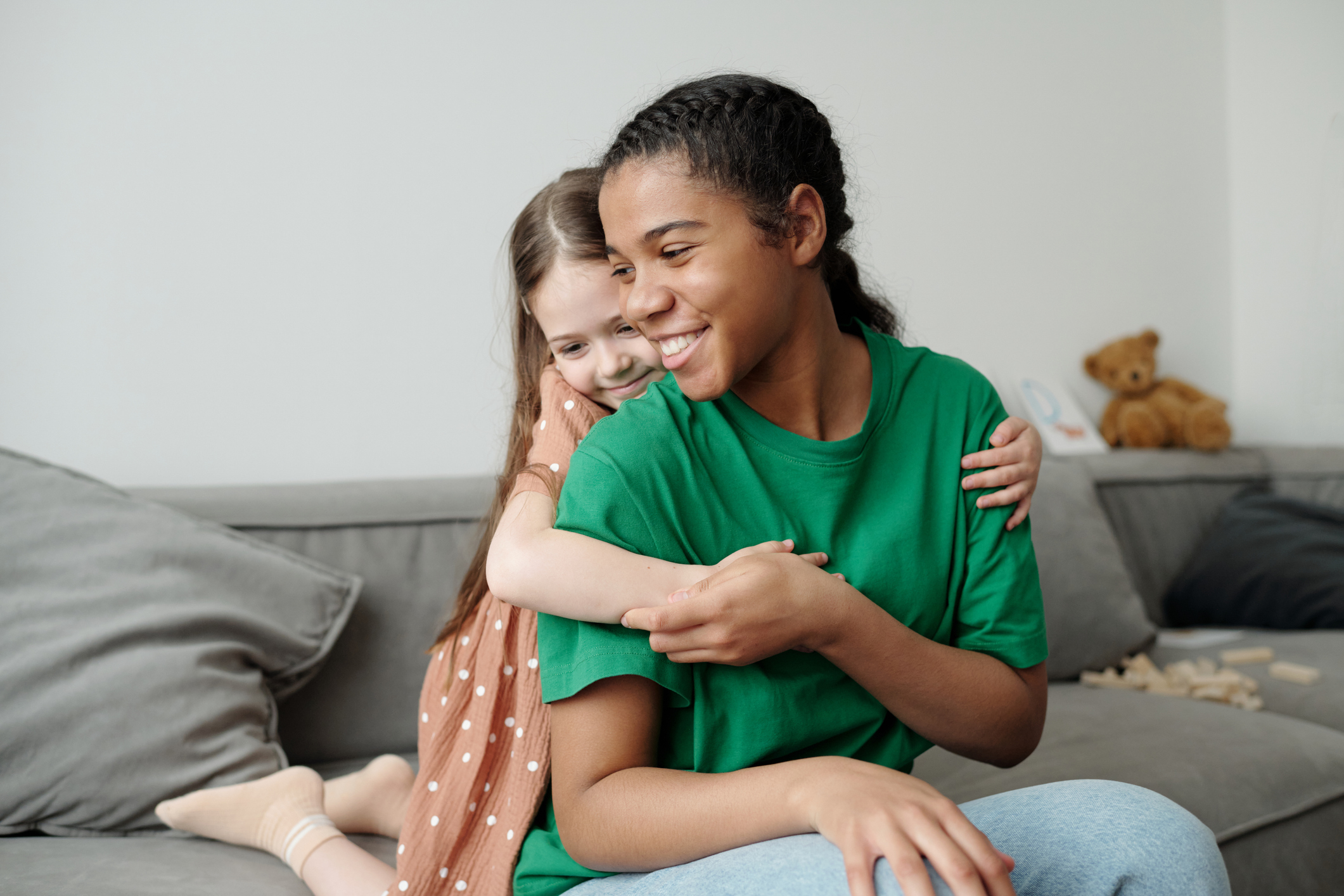 Cute cheerful African American teenager in casualwear sitting on couch and enjoying spending time with affectionate little child