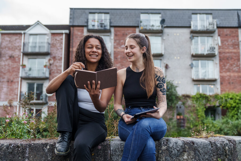 Two young women of different ethnicity with tablet and notebook having fun.