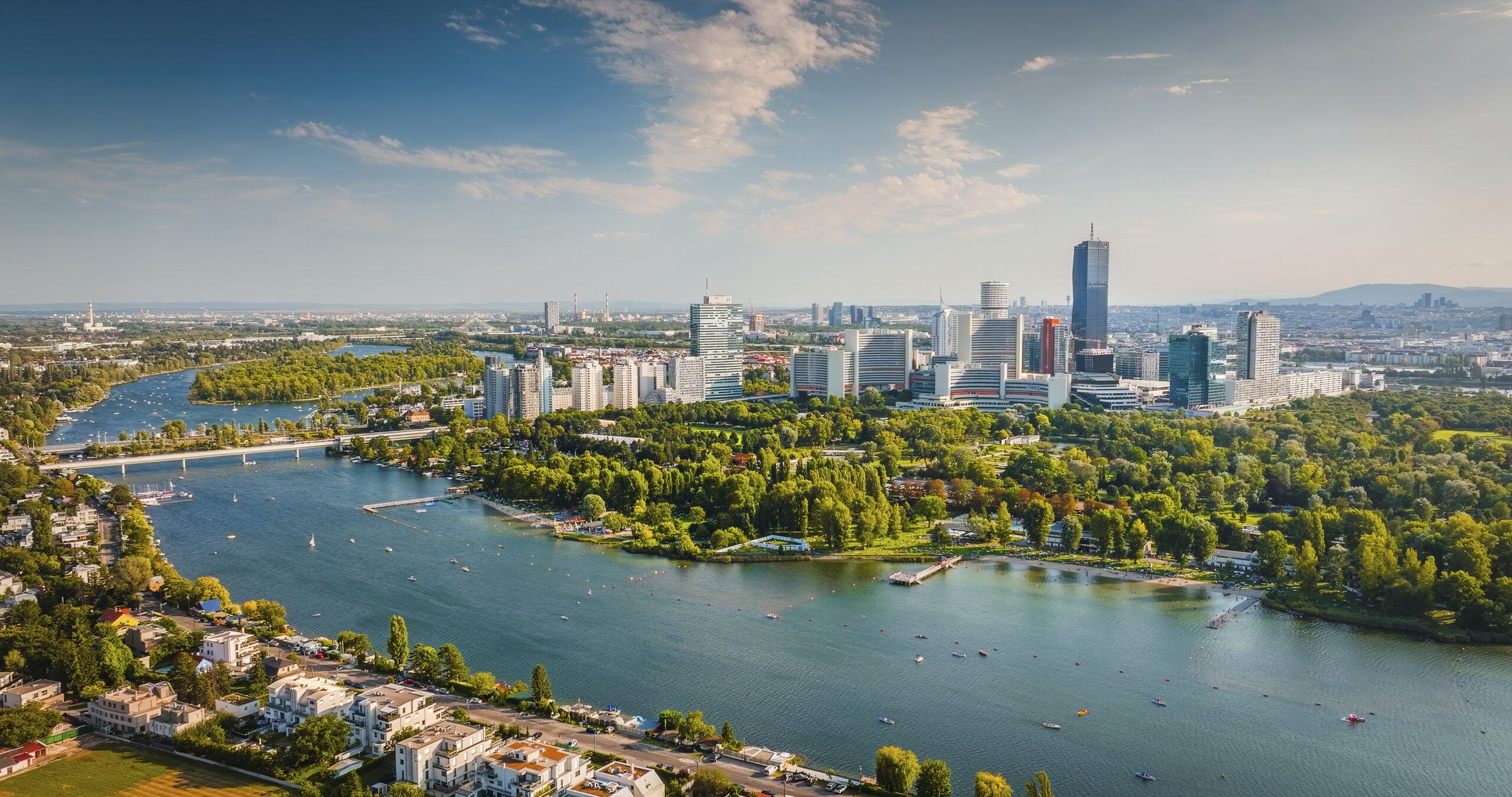 Aerial view of Vienna, Austria, showcasing the city's modern skyline including the skyscrapers of Donau City, with the Danube River and the lush greenery of the Danube Island (Donauinsel) in the foreground. Clear, sunny day. Vienna in Austria, Europe.