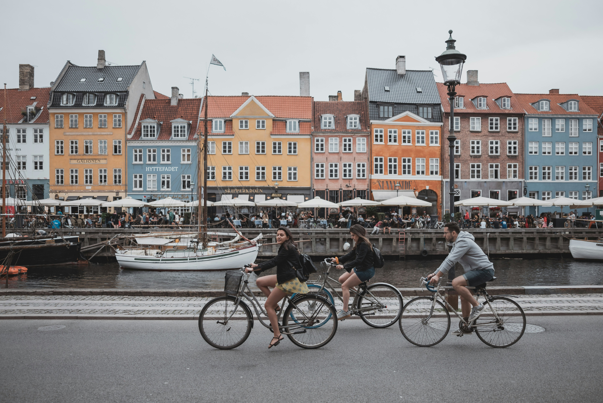 People riding bicycles in front of a canal and colorful buildings in Denamrk