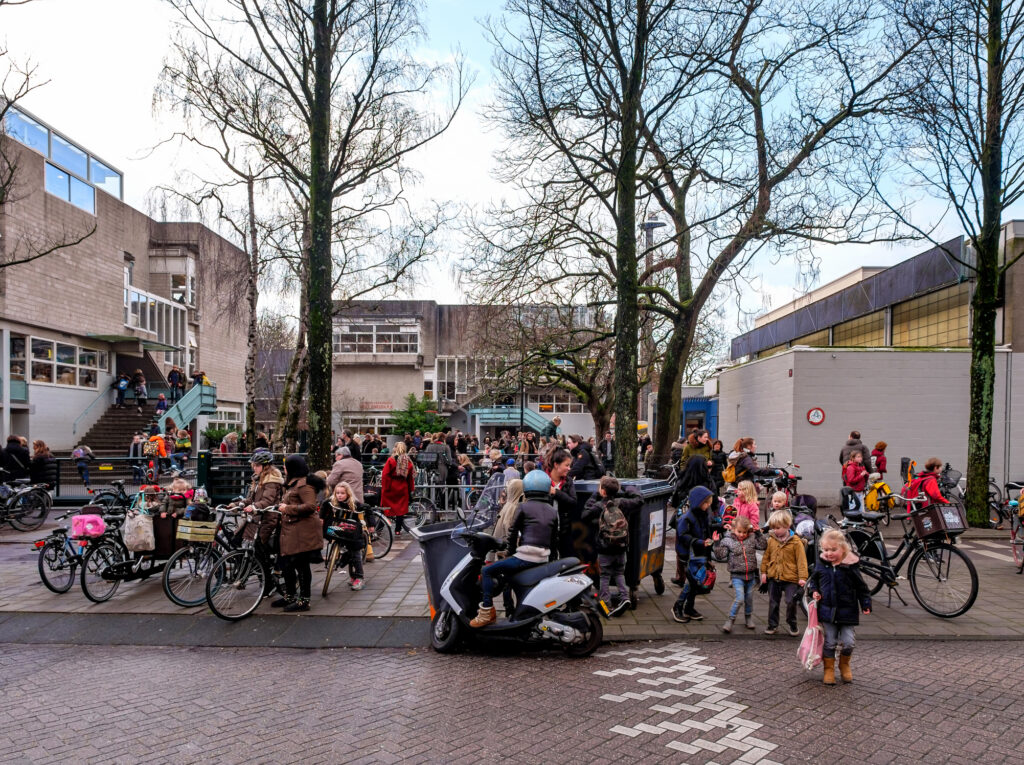 Parents on bicycles pick up their young school children at the schoolyard after school is over