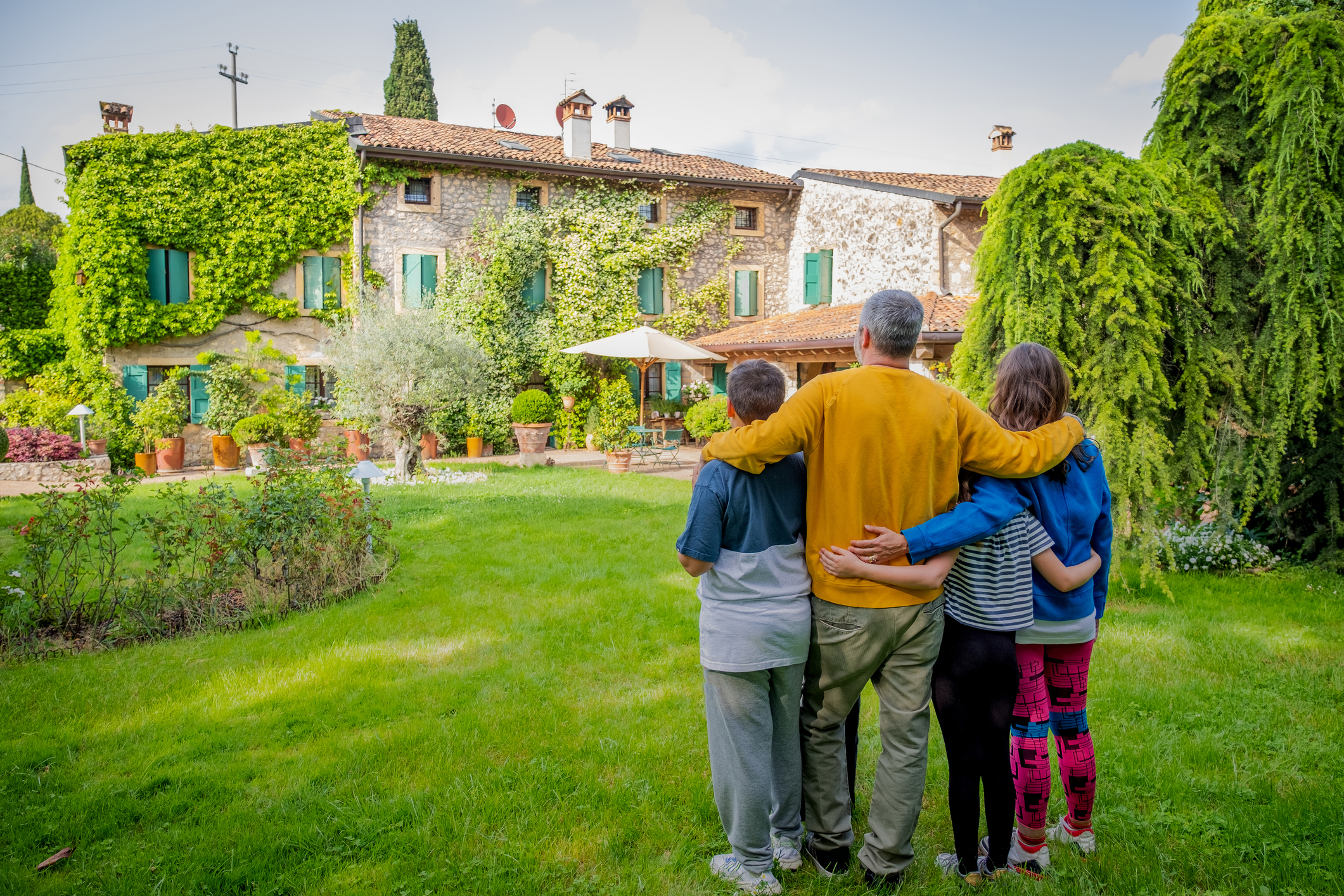Back view of happy family hugging is standing outside their new house