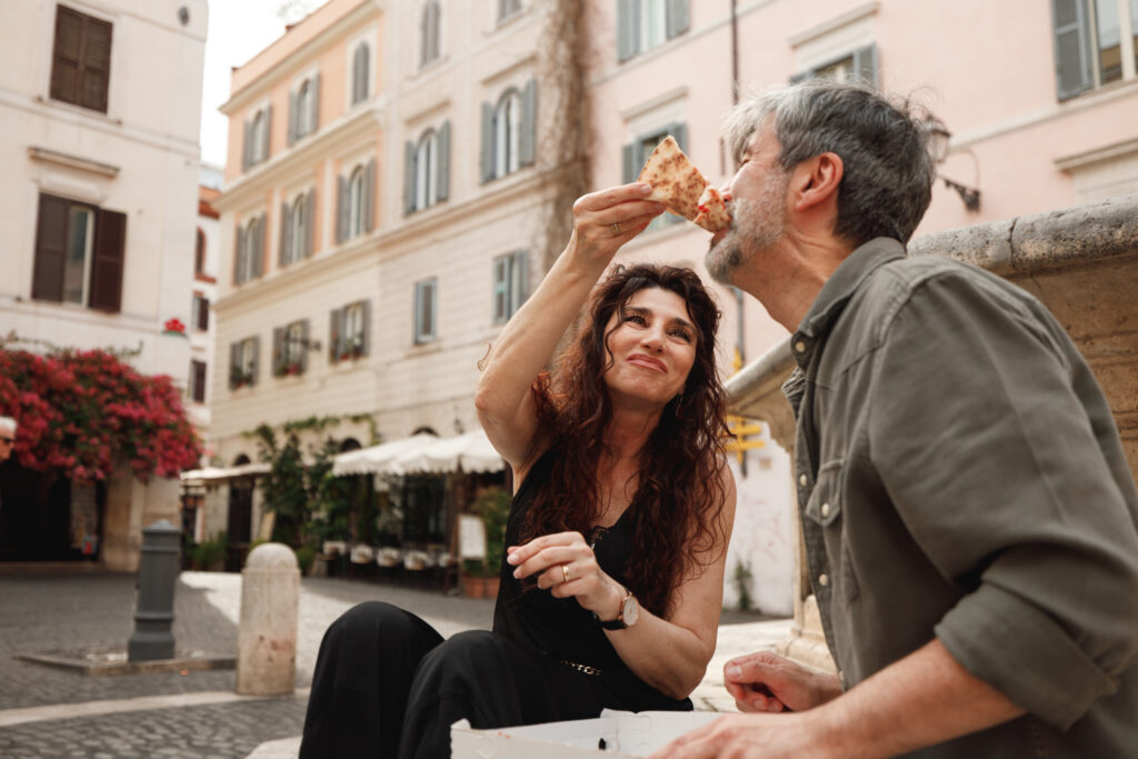 Senior couple sharing a slice of pizza in a charming Roman square